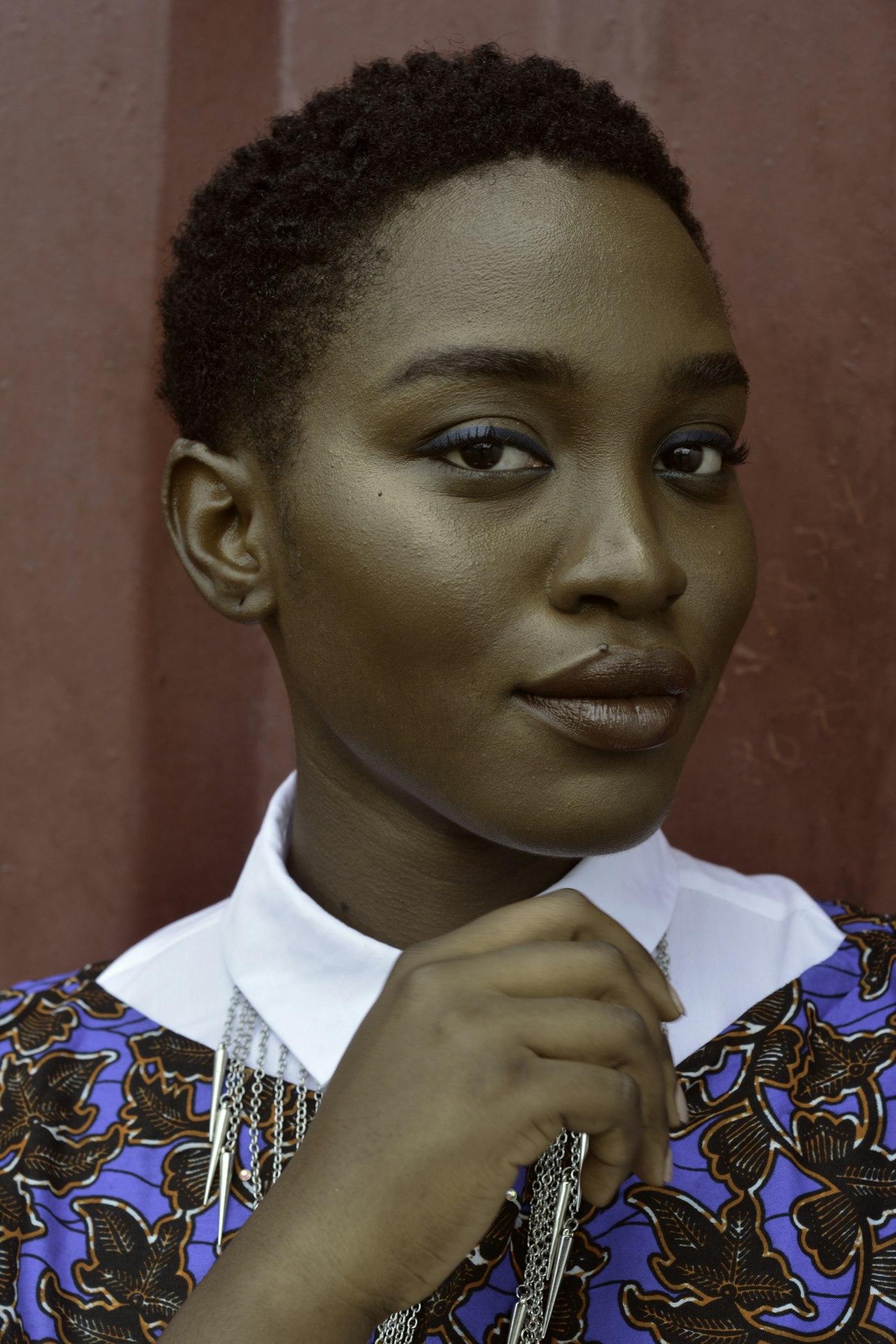 A woman in a patterned blouse, photographed against a warm wall